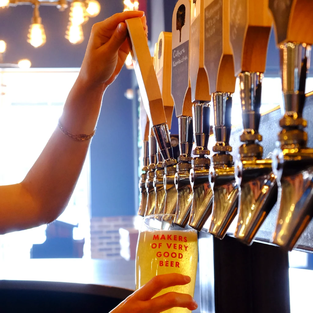 Hands pouring beer from a tap into a branded beer glass.