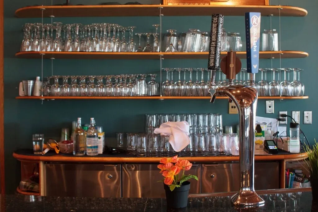Well-organized bar with shelves of glassware, a beer tap, and liquor bottles.