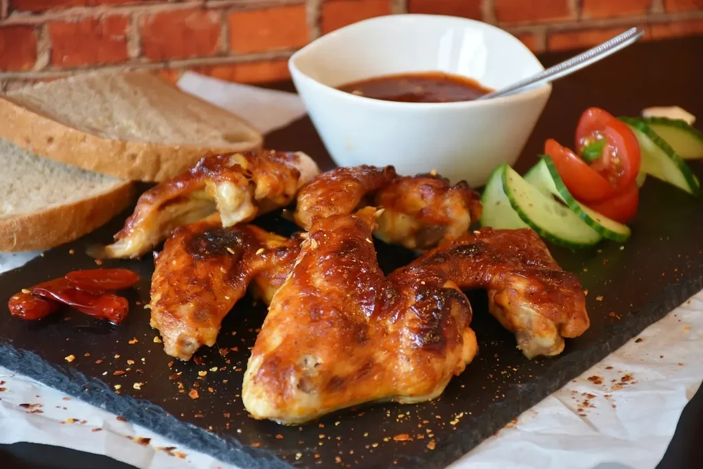 Grilled chicken wings with dark sauce on black slate, bread, and garnish.