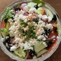 Overhead view of a Greek salad with feta in a foil container.