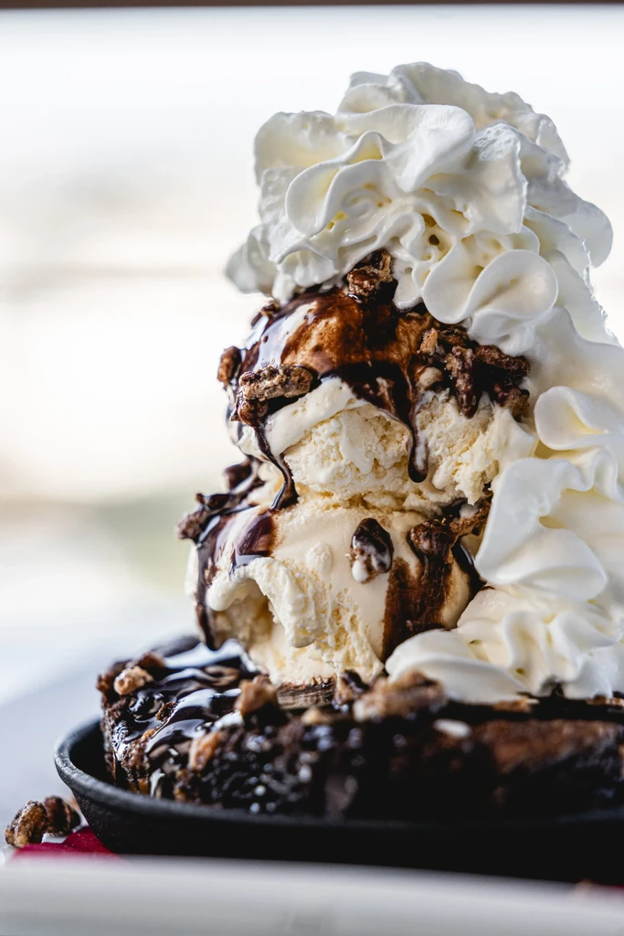 Chocolate brownie topped with vanilla ice cream, chocolate sauce, nuts, and whipped cream.
