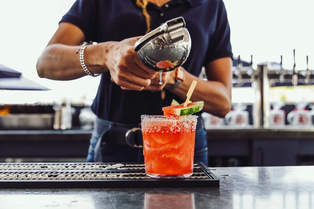 Bartender pouring a bright red watermelon cocktail at a bar.