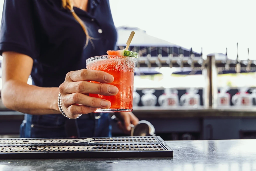 Hands holding a rimmed reddish-orange cocktail with watermelon.