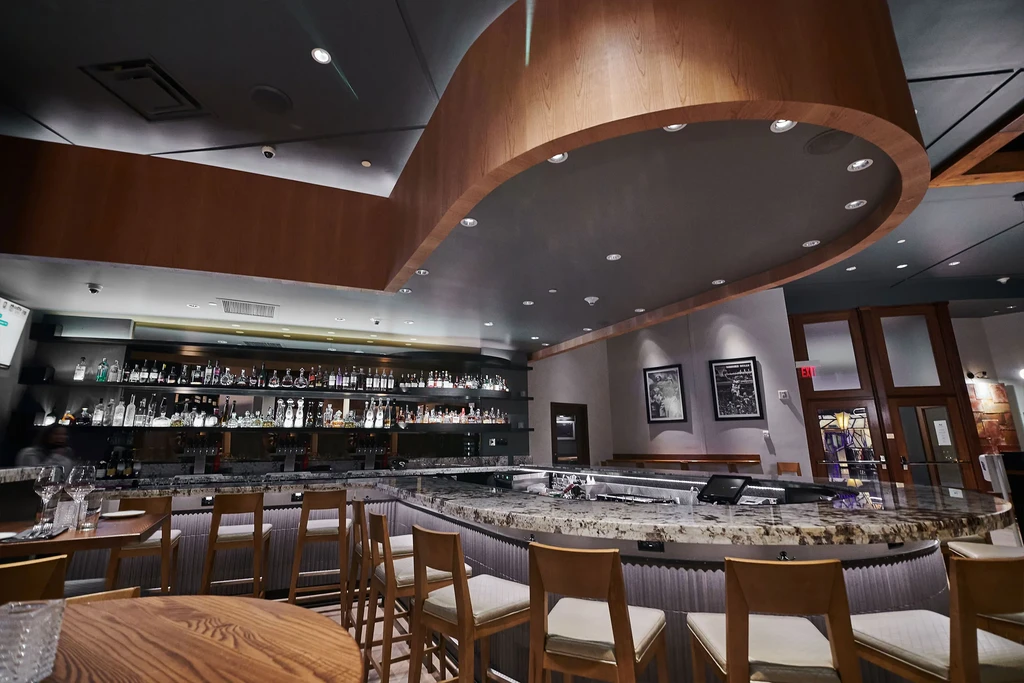 Well-lit L-shaped bar with liquor display and curved wooden ceiling.