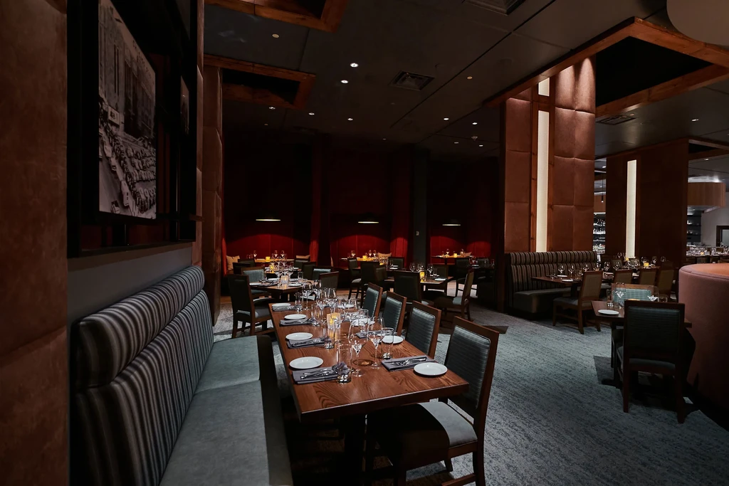 Dimly lit upscale restaurant with red walls, booths, and set tables.
