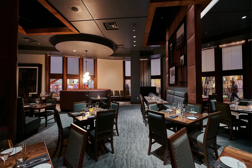 Sophisticated restaurant interior with set tables, dark wood, and warm lighting.