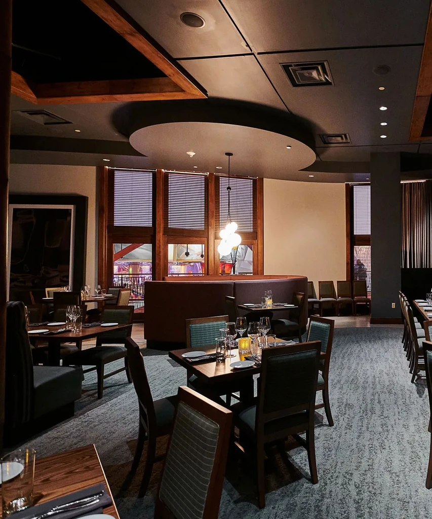 Modern restaurant interior with set tables, dim lighting, and layered ceiling.