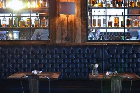 Dimly lit restaurant features leather booth, wooden wall, and liquor shelves.