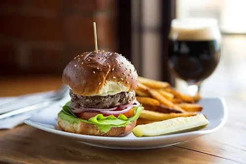 Stacked burger, golden fries, pickle spear, and dark beer.