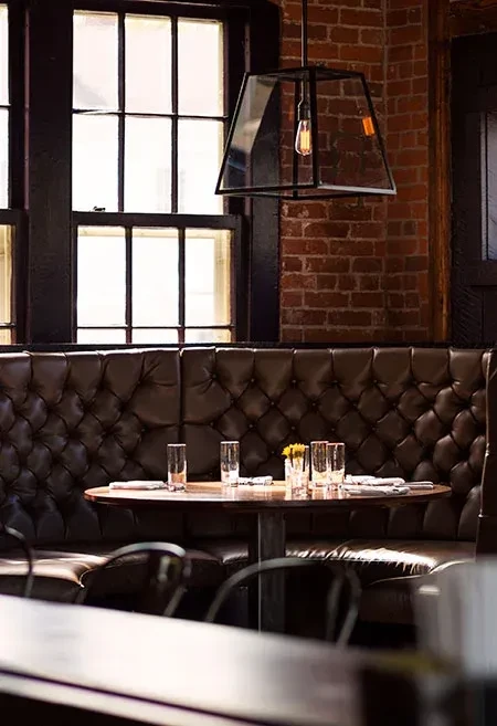 Restaurant corner: wooden table, tufted leather booth, brick wall.