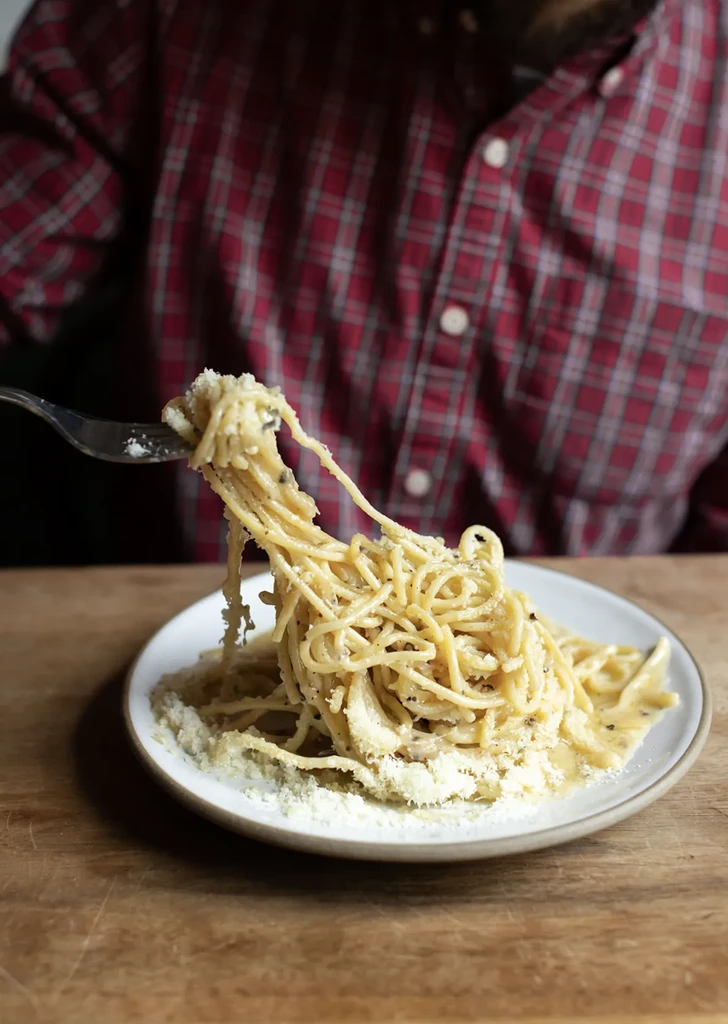 Close-up of a fork lifting creamy spaghetti with cheese and pepper.