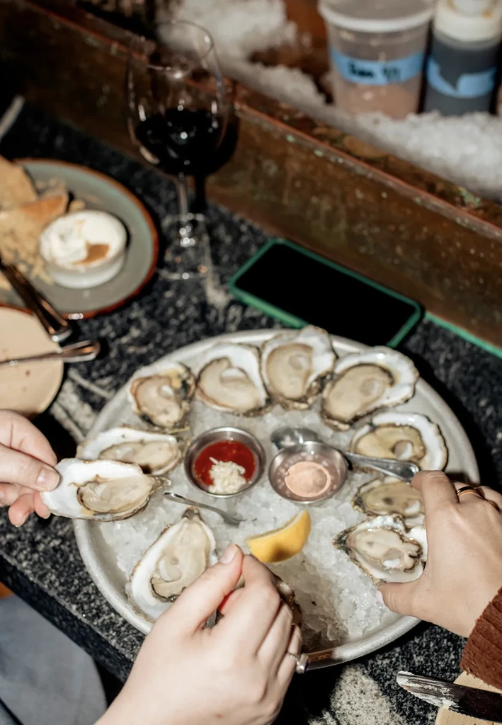 Close-up of oysters on ice, with hands reaching for them.