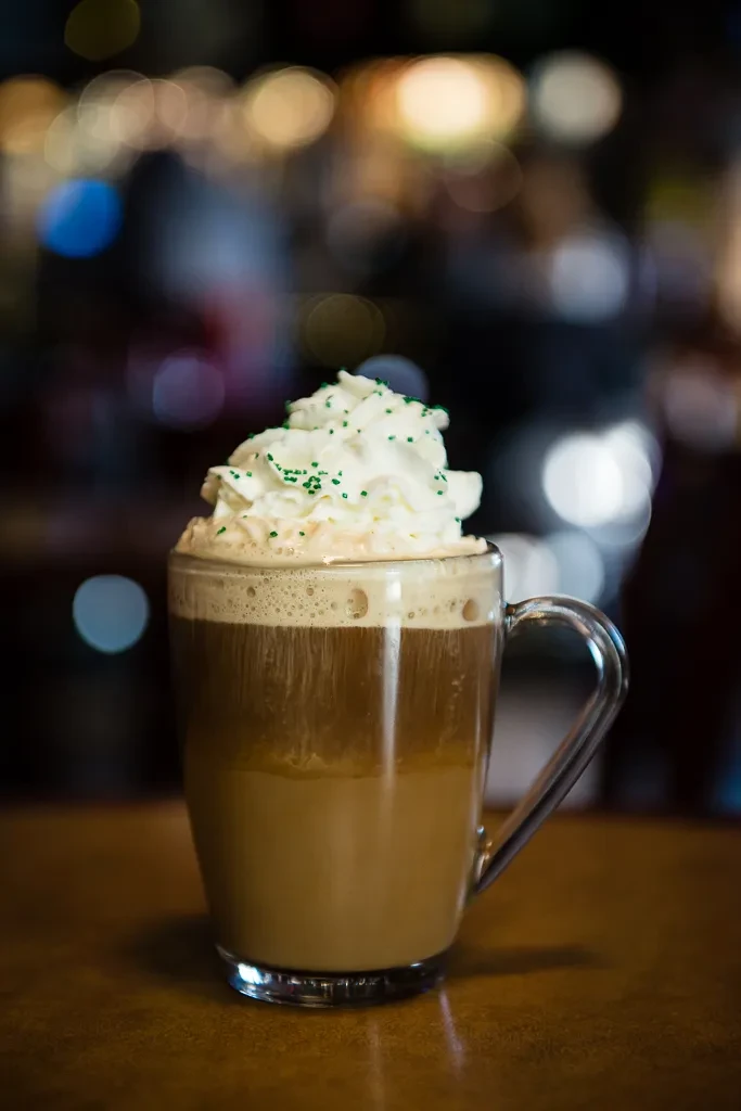 Glass mug with layered frothy brown drink, whipped cream, sprinkles.