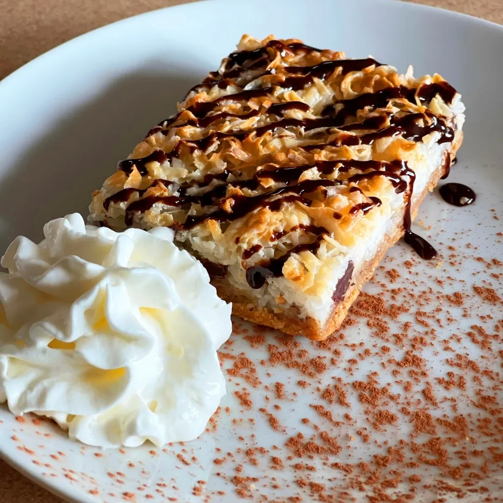 Close-up: Layered coconut dessert with chocolate drizzle and whipped cream.