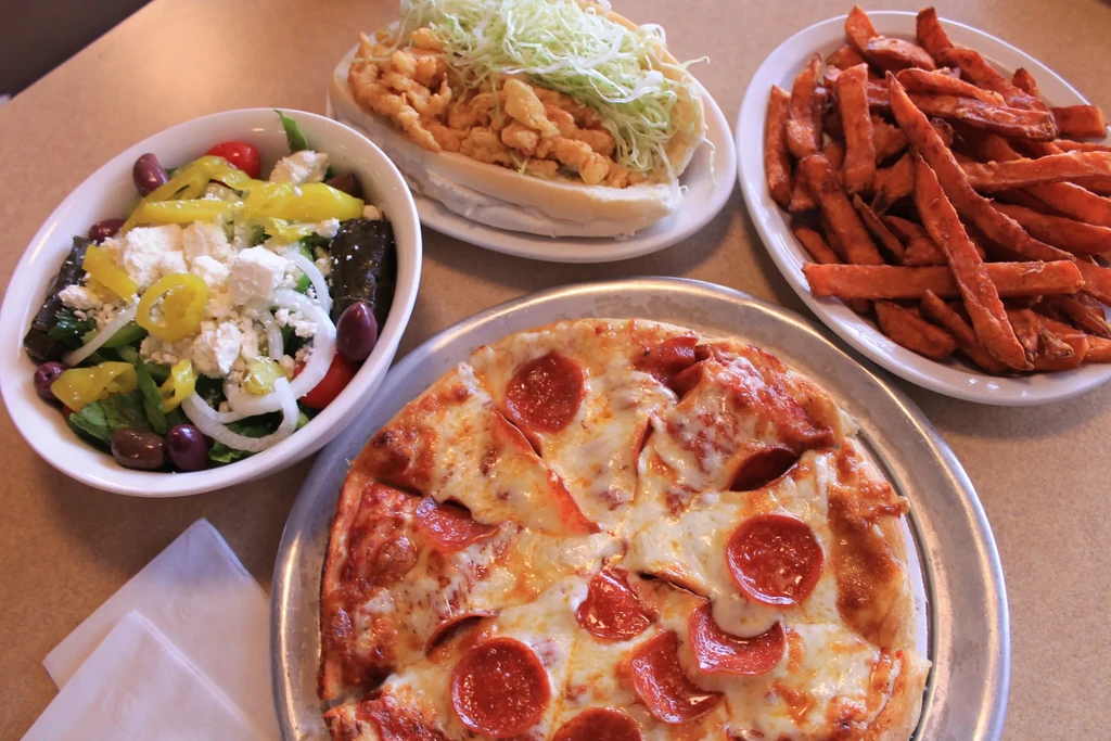 Overhead view of pizza, Greek salad, seafood sandwich, and sweet potato fries.