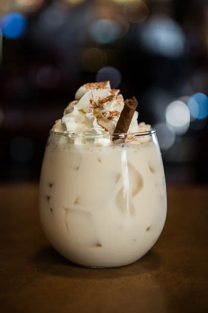 Glass of creamy white drink with ice, whipped cream, and cinnamon.