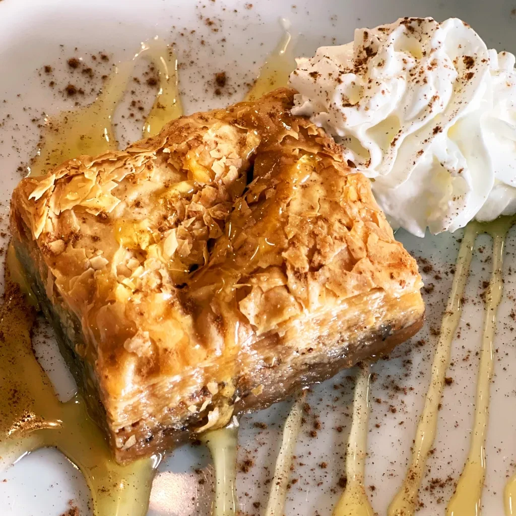 Flaky golden pastry with drizzled syrup, whipped cream, and spice.