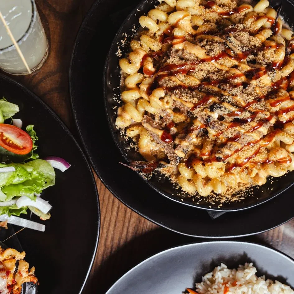 Overhead: Mac and cheese with pulled meat, salad, drink on wooden table.