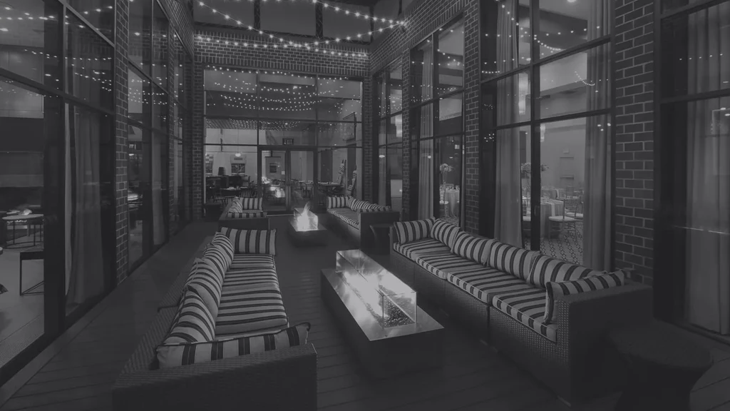Monochrome outdoor lounge with striped sofas, fire pits, and string lights.