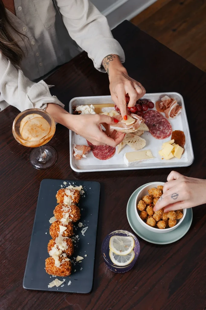 Top-down view of hands sharing charcuterie, fried bites, and cocktails.