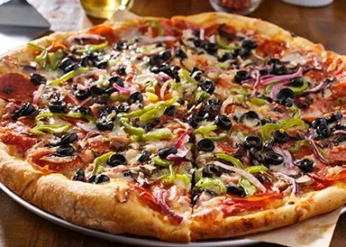 Heavily topped pizza with olives, peppers, onion, pepperoni on metal tray.