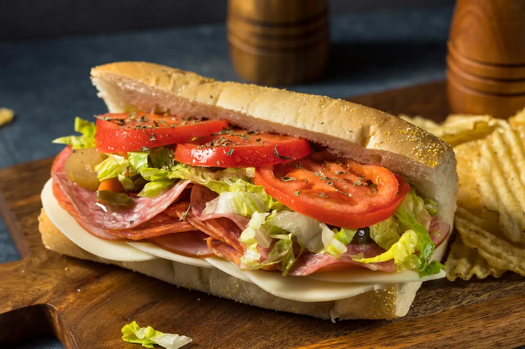 Submarine sandwich with deli meats, cheese, vegetables, and potato chips.