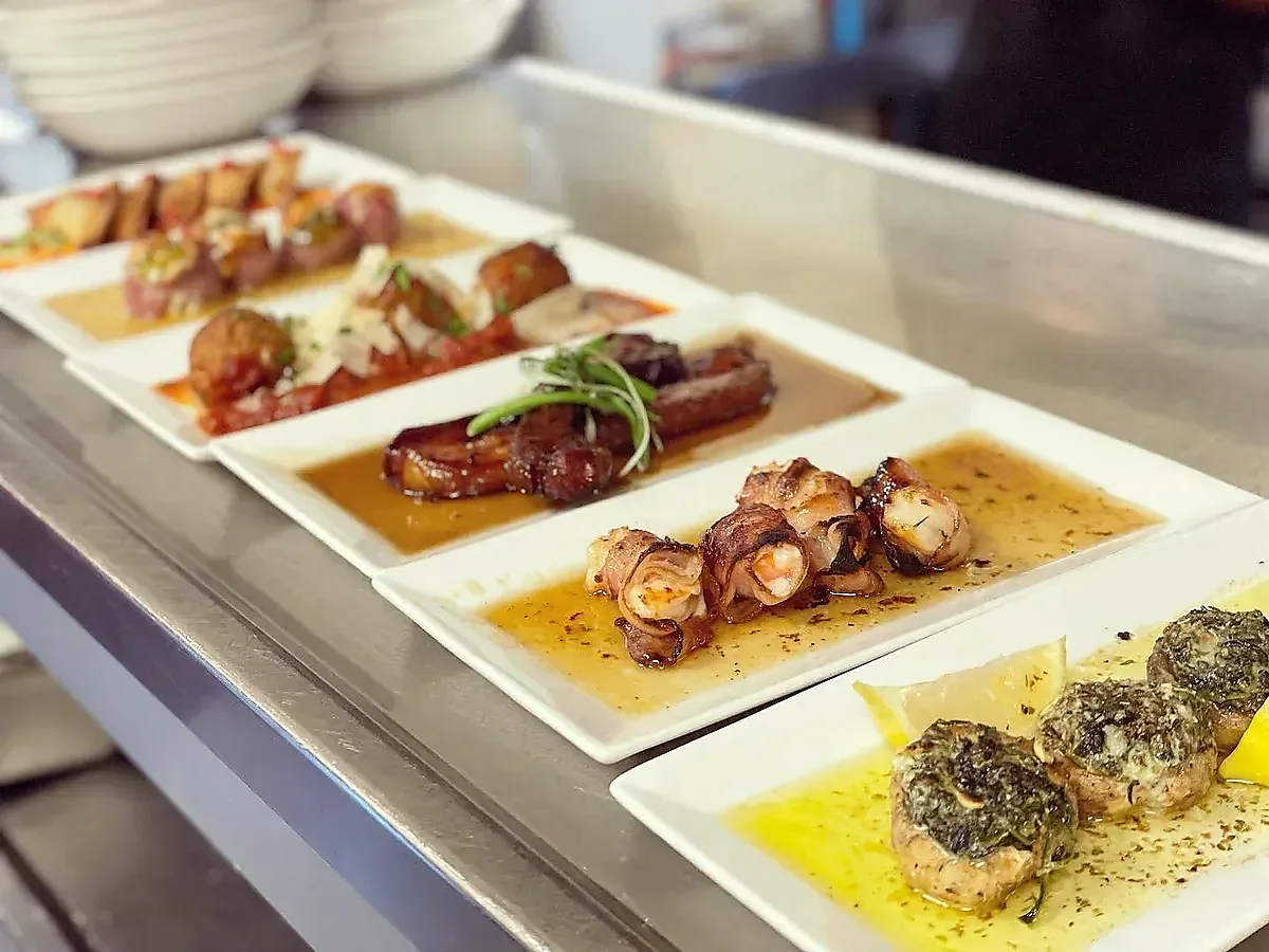 Professional serving line displays prepared dishes: mushrooms, shrimp, and meatballs.