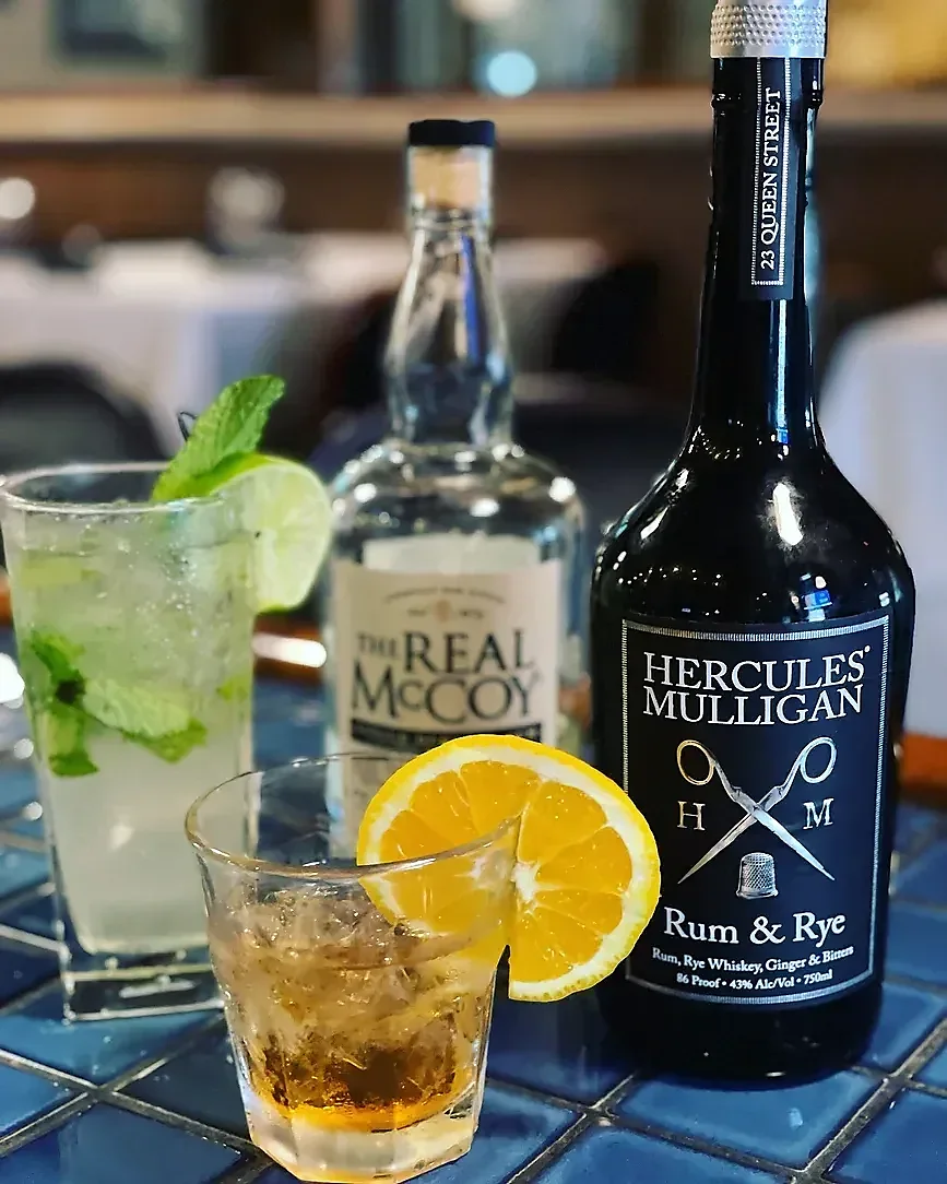 Two cocktails, "The Real McCoy" and "Hercules Mulligan" spirit bottles.