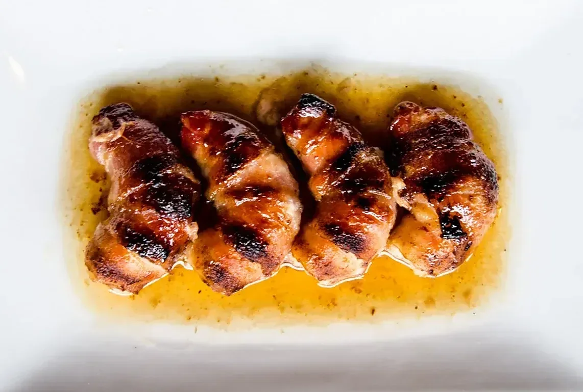 Four grilled cylindrical items with dark grill marks and golden sauce.