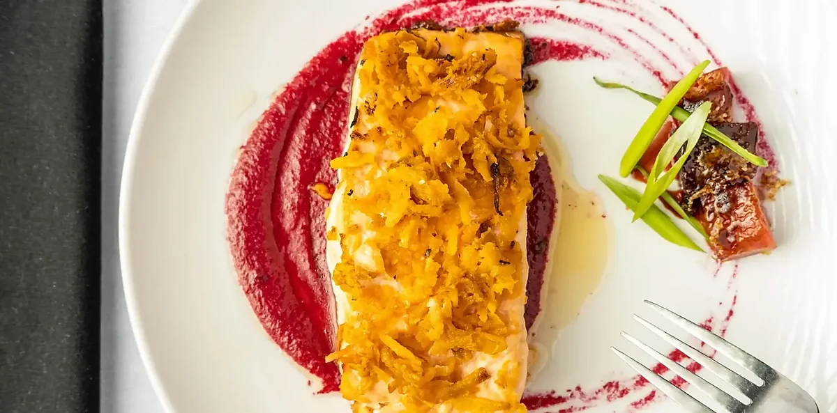 Plated fish with crispy topping, magenta purée, and meat garnish.