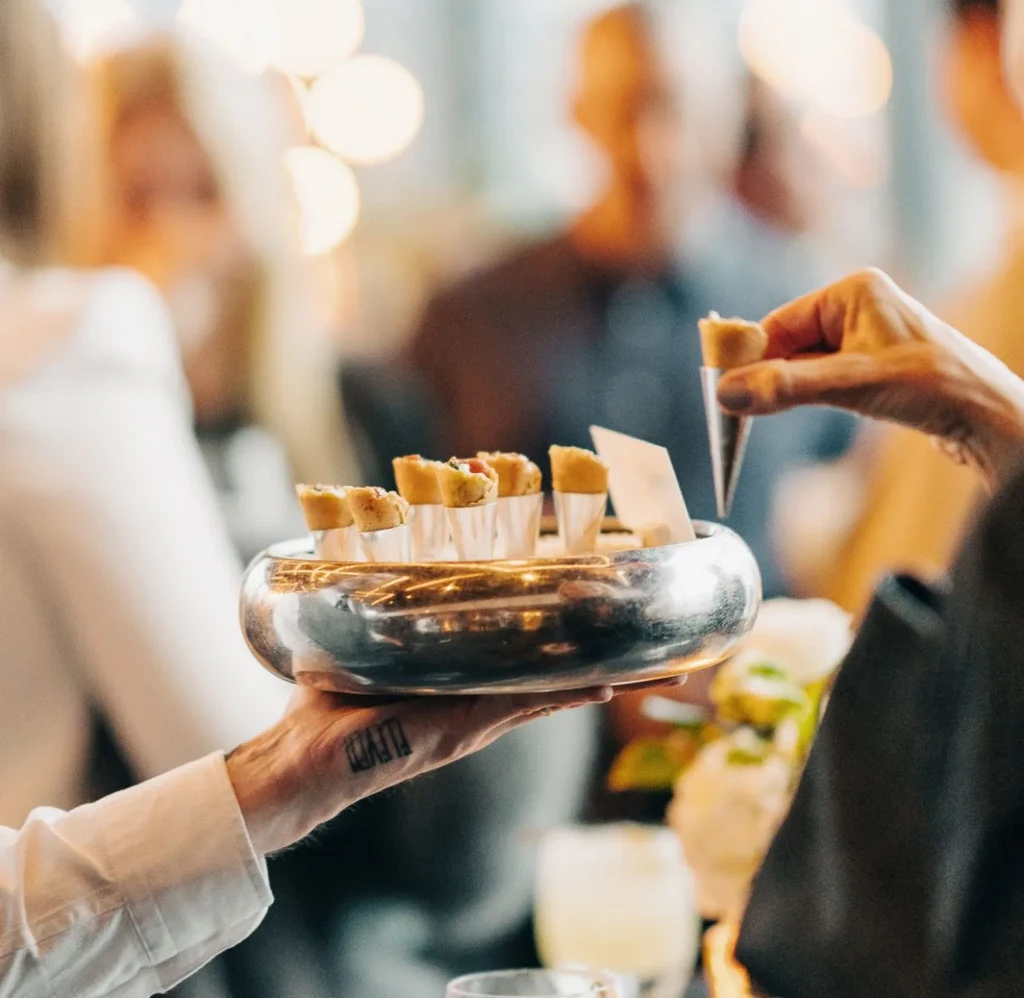 Server holding bowl of appetizers; patron's hand picks one.