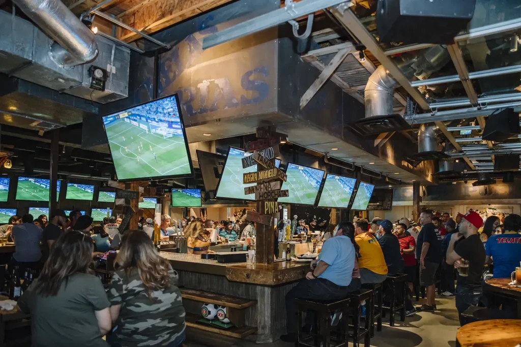 Interior of a lively sports bar with patrons watching soccer.