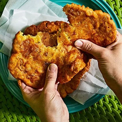 Hands pull apart a golden-brown fritter, revealing its soft interior.