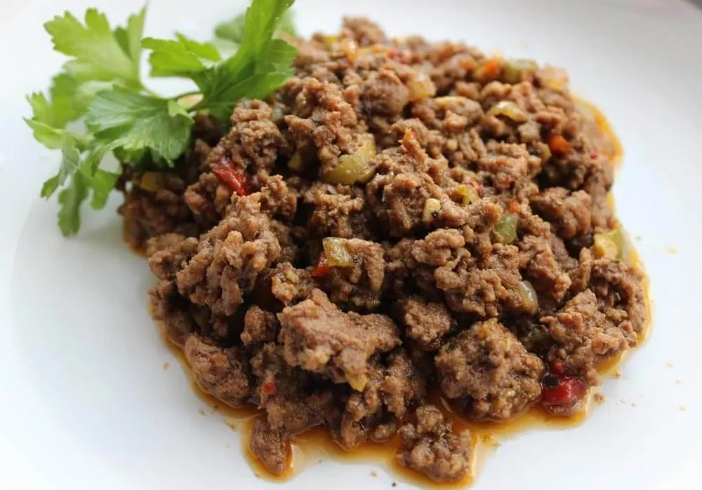 A white plate holds seasoned ground meat with parsley garnish.