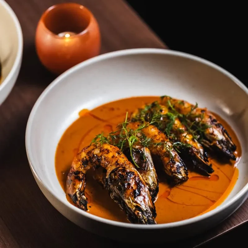 Five grilled prawns in an orange sauce, garnished with herbs.
