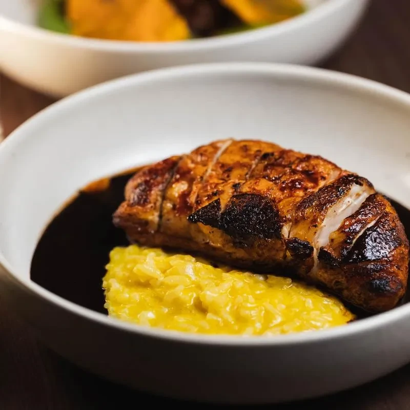 White bowl with sliced roasted meat, yellow rice, and dark sauce.