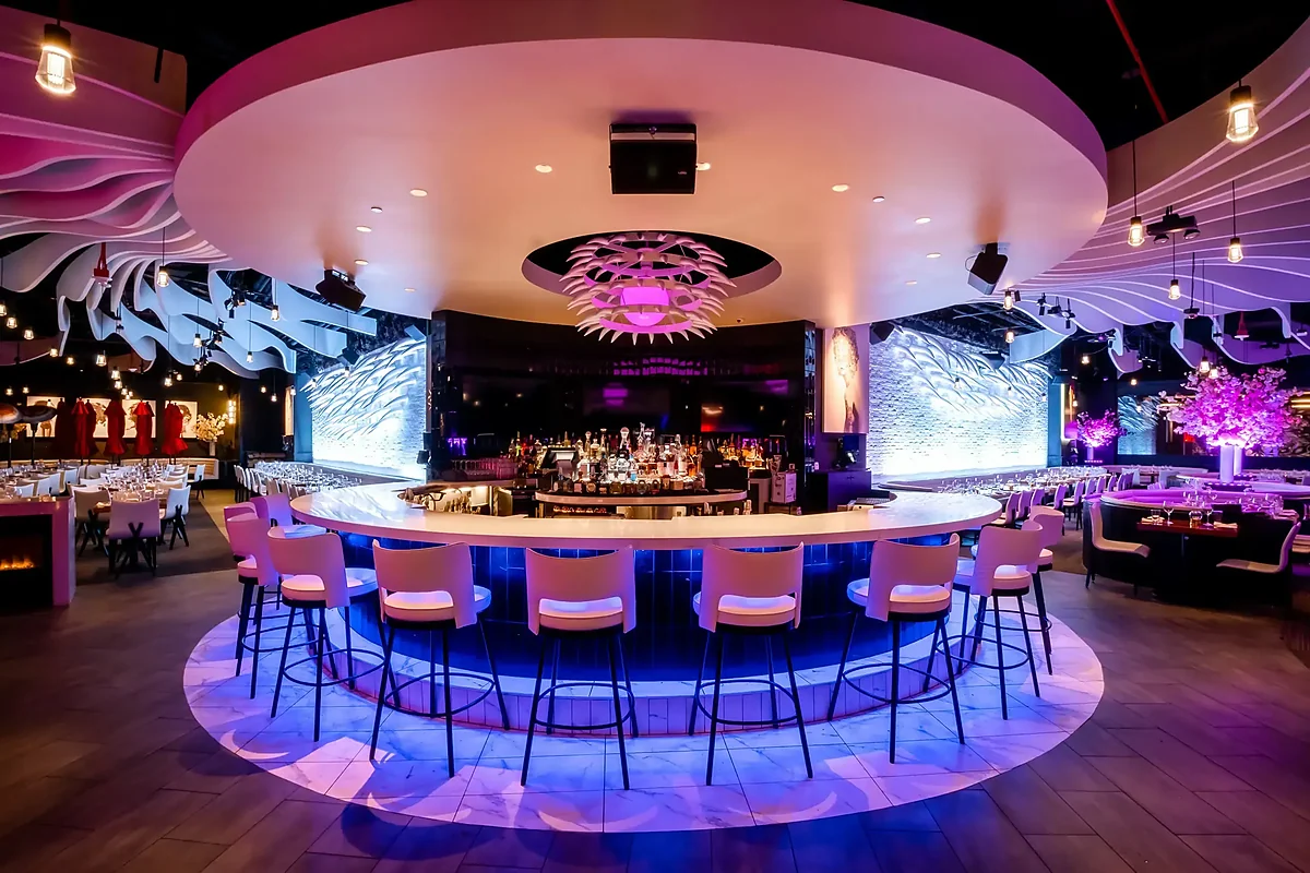 Circular white bar with barstools under pink and purple lighting