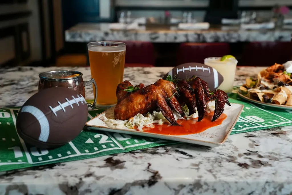 Fried chicken wings, nachos, and drinks on a football-themed table.