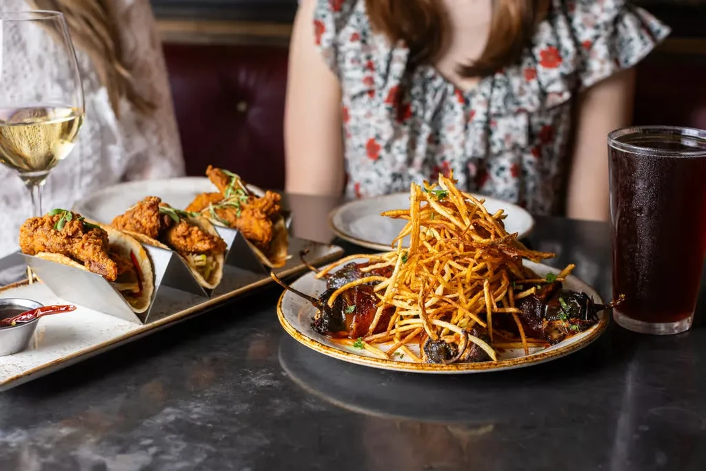 Two restaurant dishes: tacos with sauce, meat with shoestring fries.