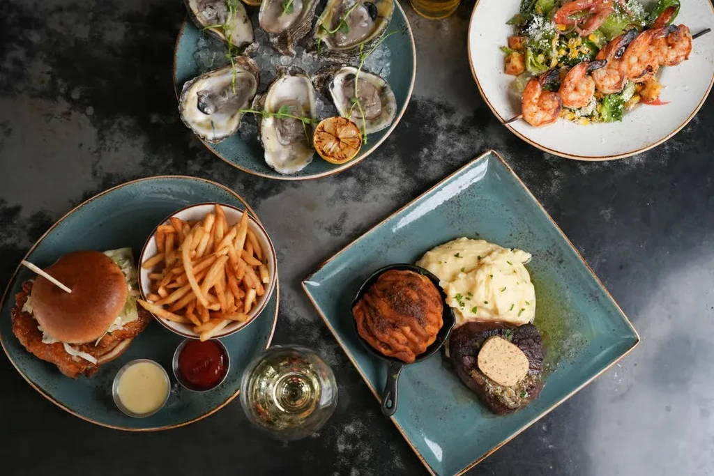 Overhead shot of a table with oysters, salad, burger, and steak.