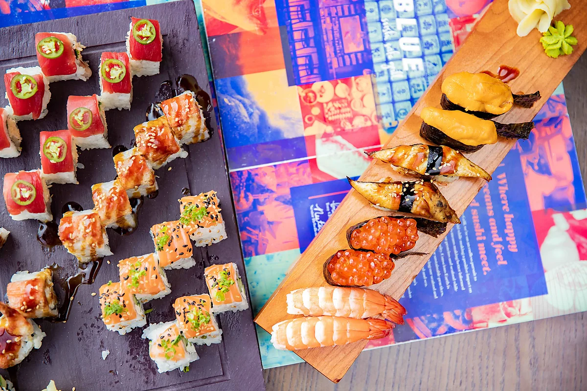 Sushi rolls on slate board beside nigiri on wooden plank