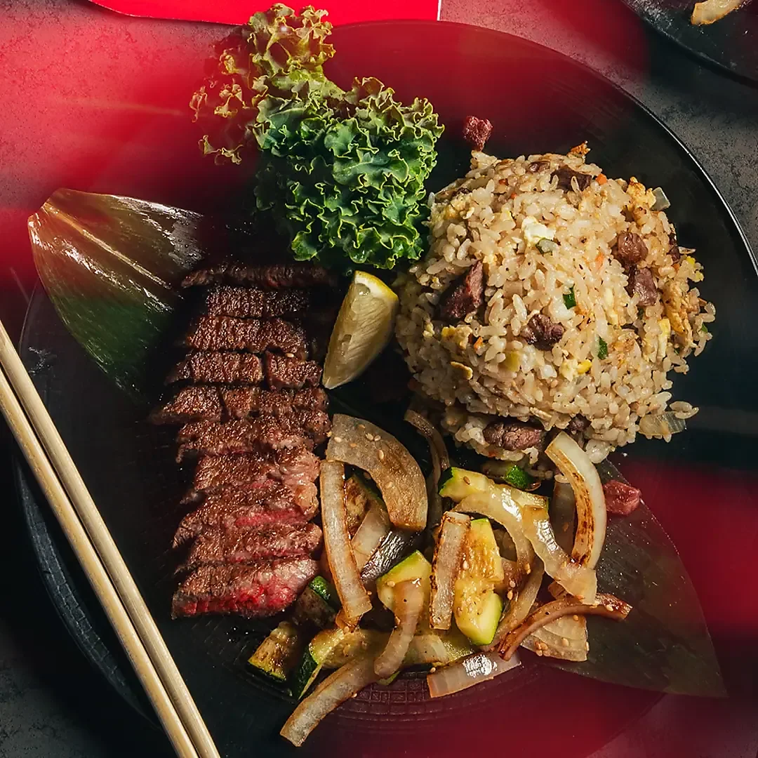 Sliced hibachi steak with fried rice, zucchini and onions on black plate