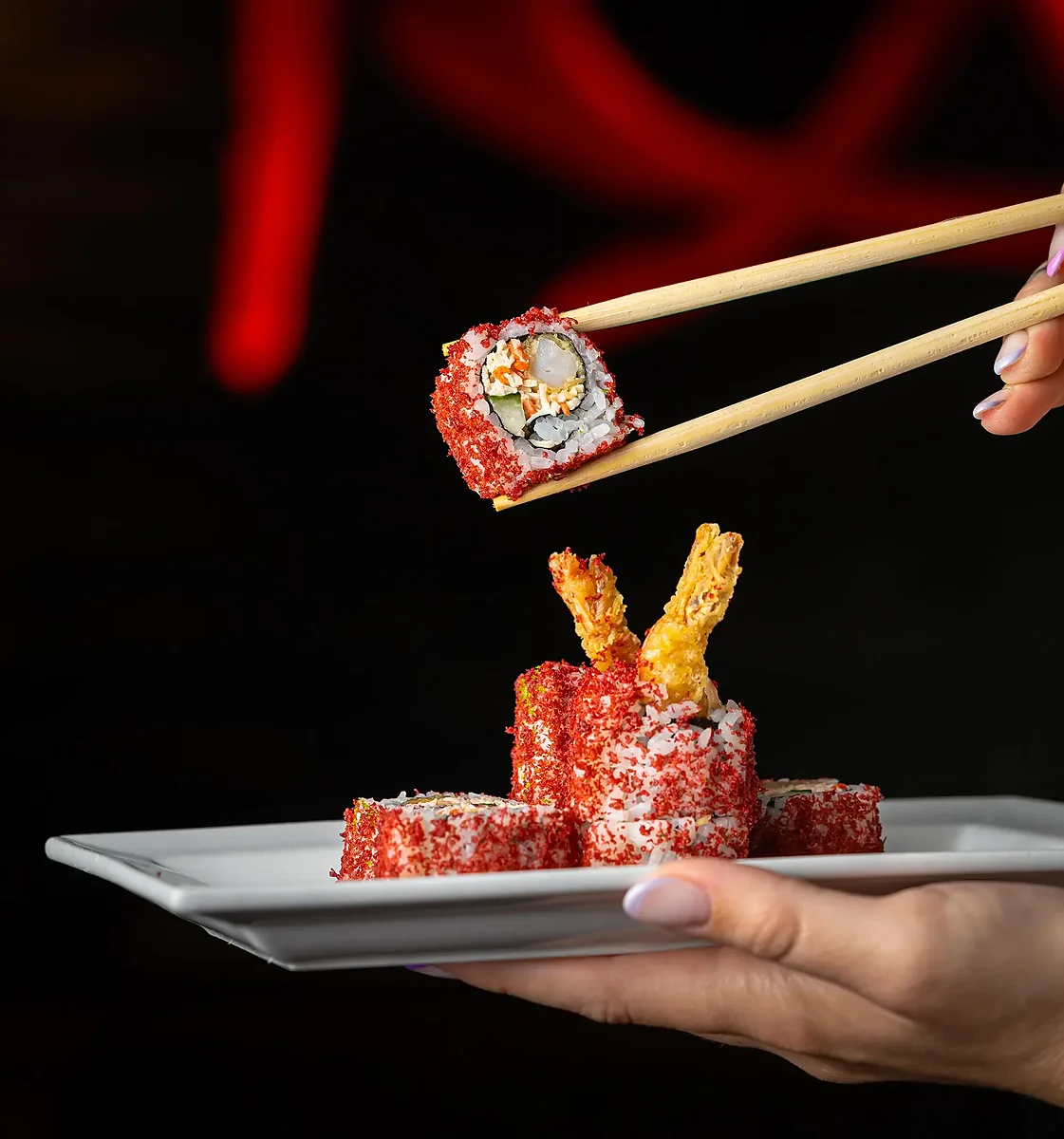 Chopsticks lifting a shrimp tempura roll from a white plate