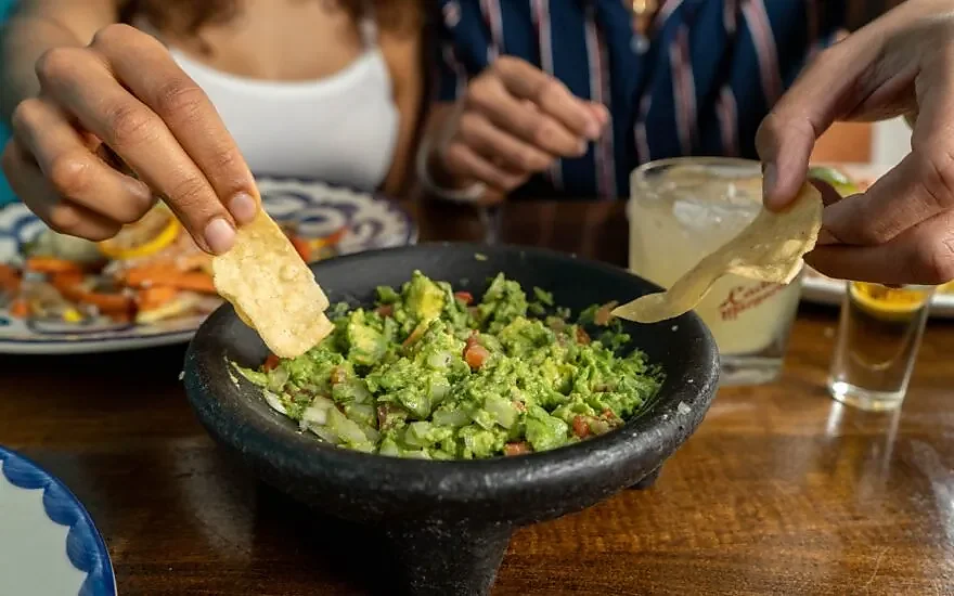 Tableside guacamole in stone molcajete with tortilla chips and margarita