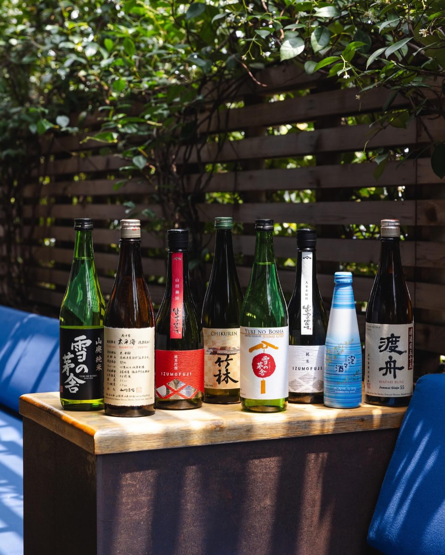Eight bottles of Japanese sake on an outdoor wooden table.