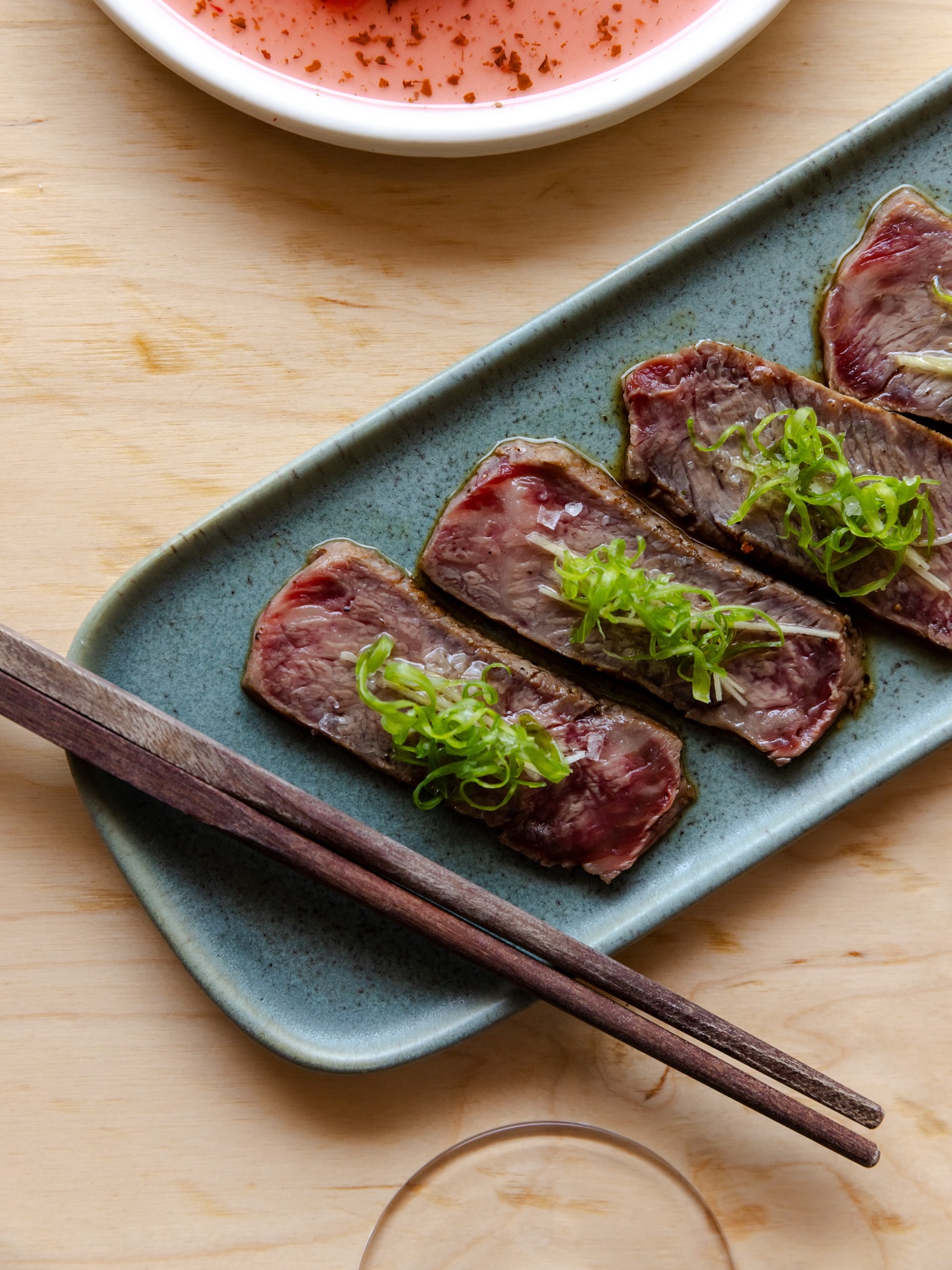 Cooked beef slices with scallions on a blue plate and chopsticks.