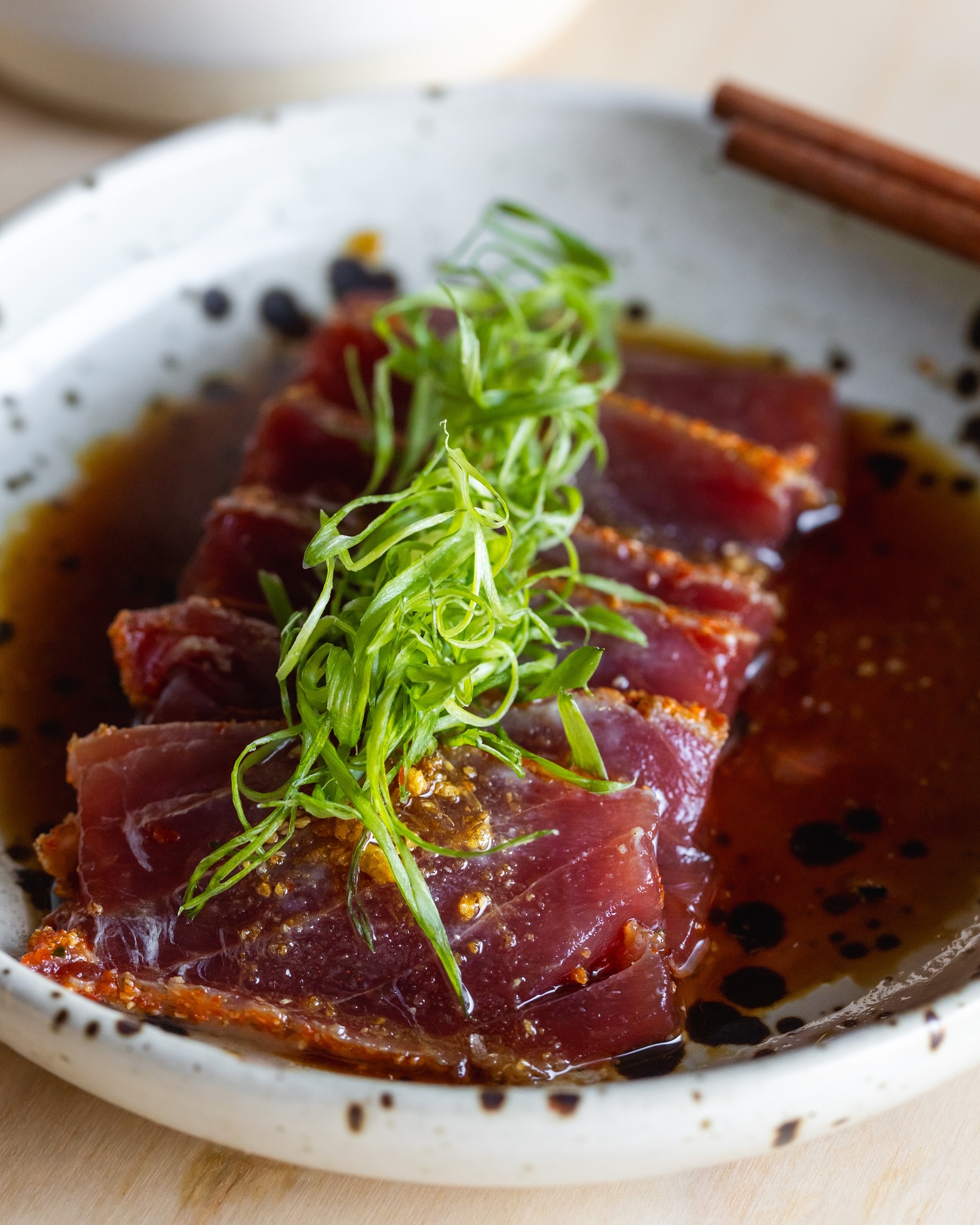 Seared tuna slices topped with green onions and dark sauce.