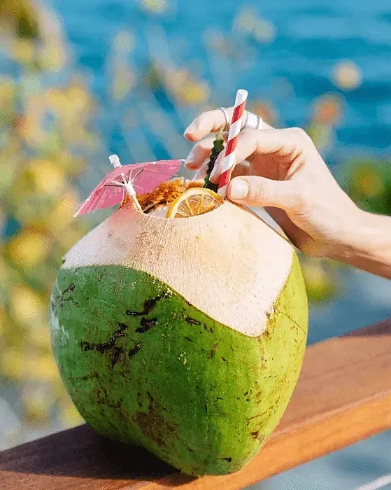 Cocktail served in a fresh green coconut beside the water