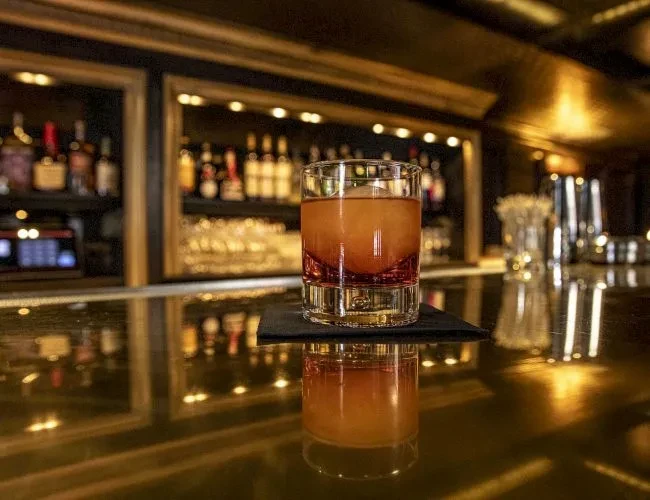 A cocktail with a large ice cube on a reflective bar counter.