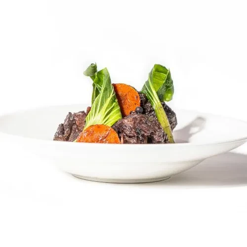 Meat stew with carrots and greens in a white bowl.